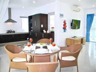 Modern dining room and kitchen area with wicker chairs, set table, and wall-mounted television