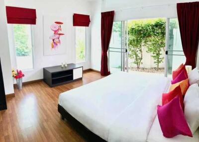 Spacious bedroom with large windows, wooden floors, and vibrant decor