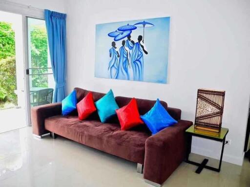 Living room with a brown sofa, colorful pillows, glass door, and wall art