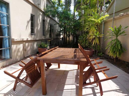 Outdoor dining area with wooden table and chairs, and lush greenery