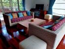 Living room with woven couches, a flat screen TV, coffee table, and large windows with blue curtains