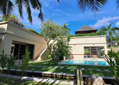 Exterior view of a house with a lawn, swimming pool, and lush vegetation