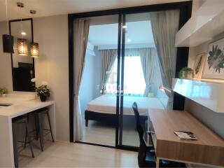 Modern studio apartment with bed, desk, and kitchen area