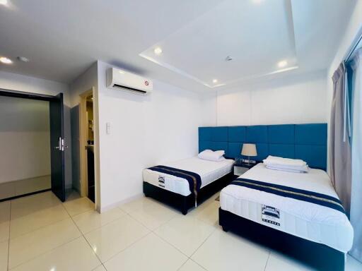 Modern bedroom with two single beds, blue headboards, and tiled floor