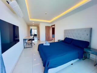 spacious bedroom with modern furnishings including a large bed, desk, and a flat-screen TV