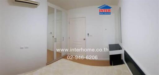 Bedroom with white walls, mirrored wardrobe, air conditioner, and minimal furnishing.