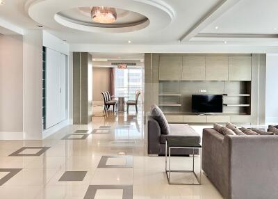 Modern living room with grey sectional sofa, wall-mounted TV, and dining area in the background