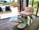 Modern living room with a glass coffee table, seating area, and large glass doors opening to a patio with a pool view.