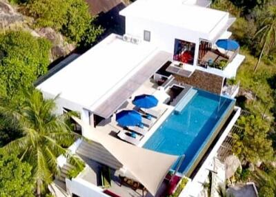 Aerial view of a modern hillside villa with a swimming pool and lush surroundings