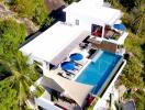 Aerial view of a modern hillside villa with a swimming pool and lush surroundings