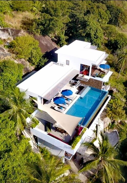 Aerial view of a modern hillside villa with a swimming pool and lush surroundings