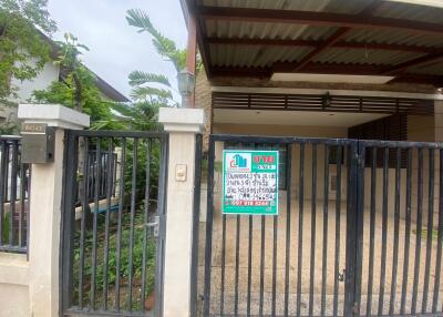 Front view of a residential property with a gated entrance, covered carport, and signage