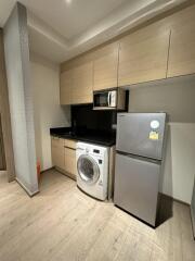 Modern kitchen with wooden cabinetry, washing machine, microwave, and fridge