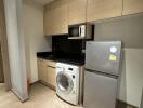 Modern kitchen with wooden cabinetry, washing machine, microwave, and fridge