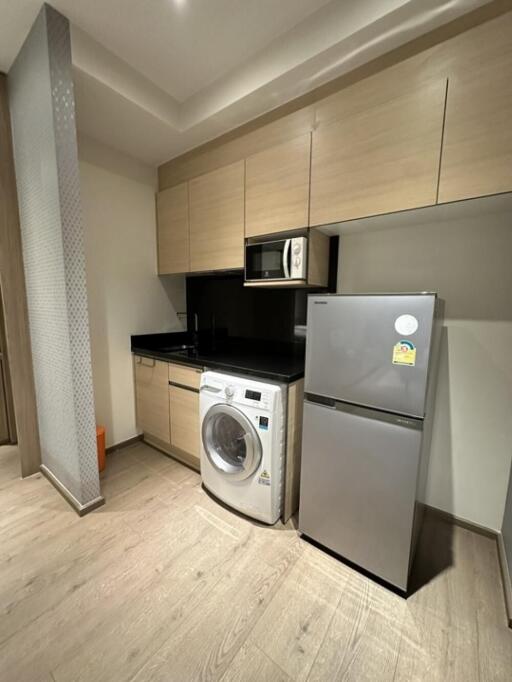 Modern kitchen with wooden cabinetry, washing machine, microwave, and fridge