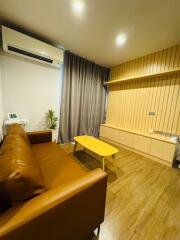 Modern living room with a brown leather sofa, wooden coffee table, air conditioning unit, and wall-mounted wooden paneling.