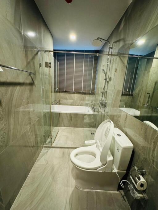 Modern bathroom with sleek gray tiles, bathtub, toilet, and glass shower enclosure
