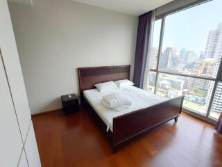 Bedroom with large window offering city view, wooden floor, and a double bed with side table