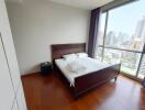 Bedroom with large window offering city view, wooden floor, and a double bed with side table