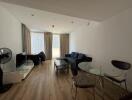 Modern living room with wooden flooring, a dark sectional sofa, and a glass dining table