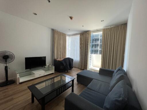 Spacious living room with a modern furnishing, including a large sofa, coffee table, TV setup, and large windows with curtains.