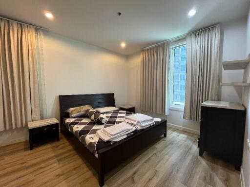 Bedroom with wooden floor, bed, nightstands, and curtains