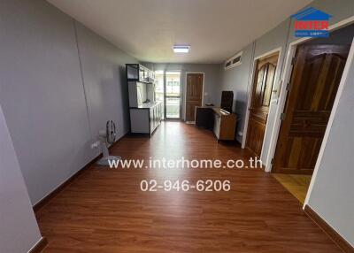 Spacious living area with wooden floor, connected to a kitchen, featuring light grey walls and wooden doors