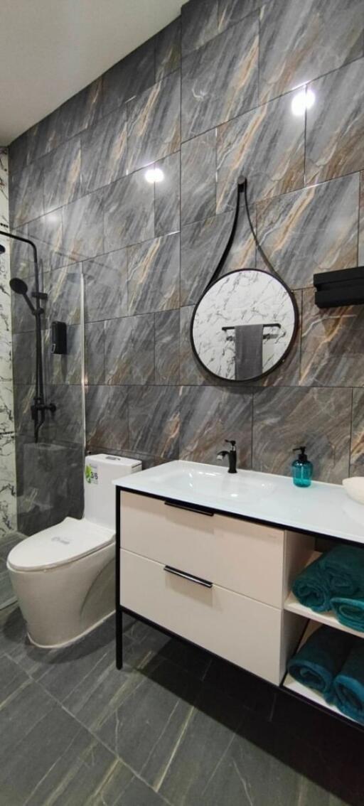 Modern bathroom with marble tile walls, a round mirror, a toilet, and a vanity with storage space