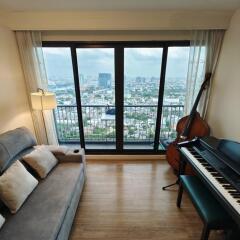 Living room with a city view, a grey sofa, a floor lamp, a double bass, and a piano with a chair