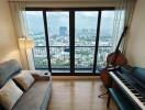 Living room with a city view, a grey sofa, a floor lamp, a double bass, and a piano with a chair