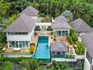 Aerial view of a luxurious villa with multiple buildings and a large swimming pool surrounded by lush greenery