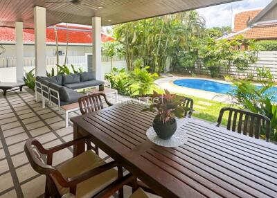 Covered outdoor living area with dining table, lounge chairs, and view of garden and swimming pool