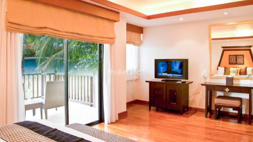 Spacious bedroom with a sliding glass door opening to a balcony, featuring a large bed, TV on a stand, wooden flooring, and ample natural light.