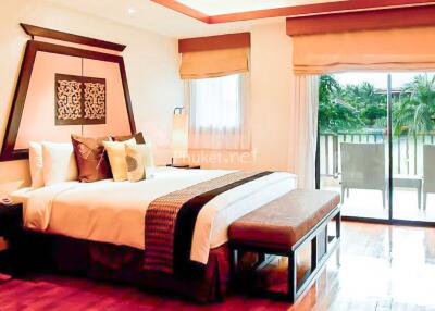 Spacious bedroom with large bed, modern decor, sliding glass door leading to a balcony with a view of greenery