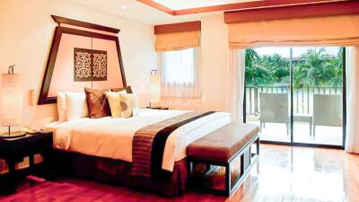 Spacious bedroom with large bed, modern decor, sliding glass door leading to a balcony with a view of greenery