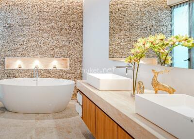 Modern bathroom with stone accent wall, freestanding bathtub, and decorative elements