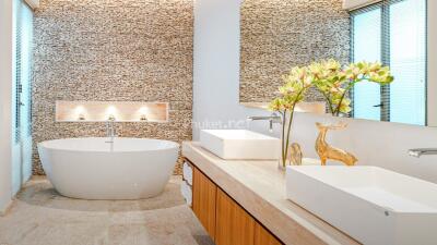 Modern bathroom with stone accent wall, freestanding bathtub, and decorative elements