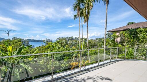 Balcony with glass railing overlooking lush greenery and distant waterfront