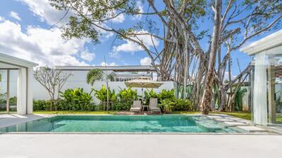 Backyard with swimming pool, sun loungers, umbrella, and lush greenery