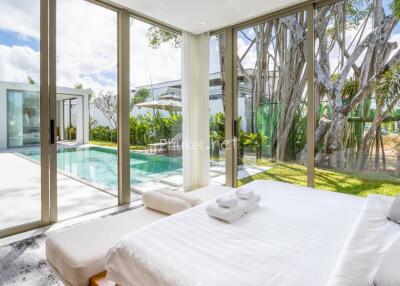 Spacious bedroom with large glass windows offering a view of the pool and garden