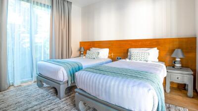 Modern bedroom with two single beds, wooden headboard, and large window with curtains