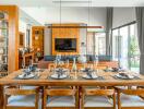 Modern dining room with wooden table and chairs, set up for a meal, connected to living area with TV and large windows.