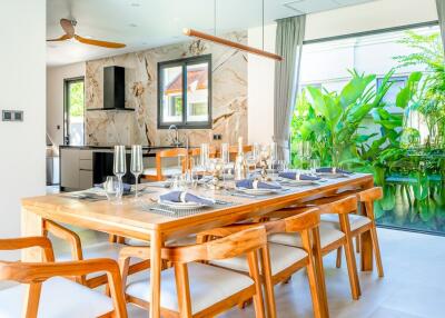 Modern dining room with wooden table, elegant place settings, and adjacent kitchen