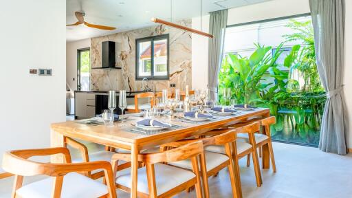 Modern dining room with wooden table, elegant place settings, and adjacent kitchen