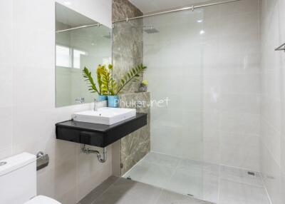 Modern bathroom with a glass shower, large mirror, and a sink with a vase of plants