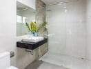 Modern bathroom with a glass shower, large mirror, and a sink with a vase of plants