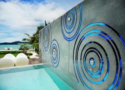 Outdoor pool area with artistic wall and beach view