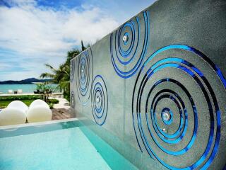 Outdoor pool area with artistic wall and beach view