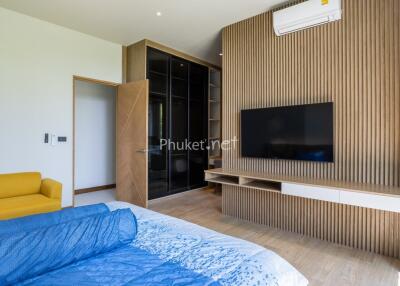 Modern bedroom with a large flat-screen TV, yellow sofa, and a wooden accent wall