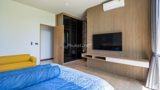 Modern bedroom with a large flat-screen TV, yellow sofa, and a wooden accent wall